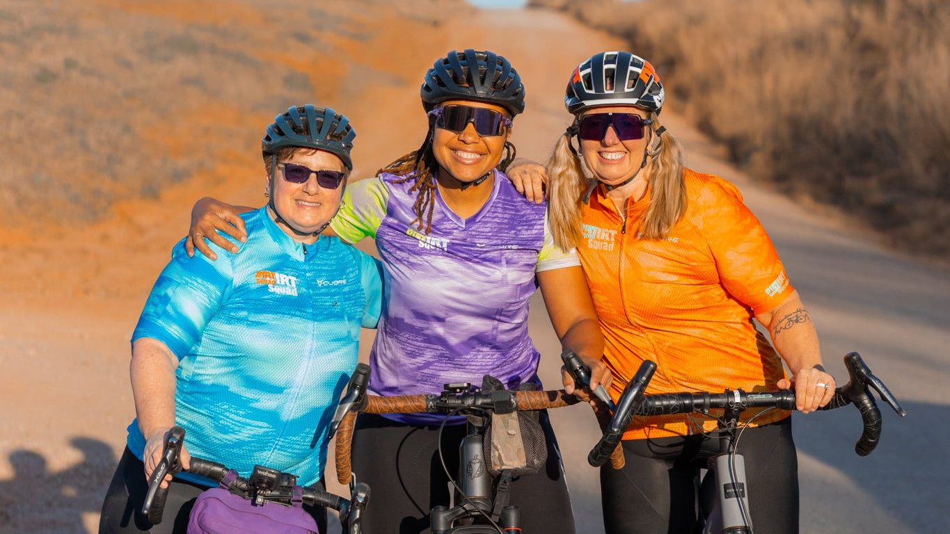 Three cyclists posing together on a road with bicycles